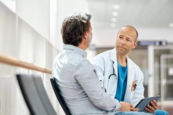 Provider speaking to a patient in a hallway. He is holding a tablet